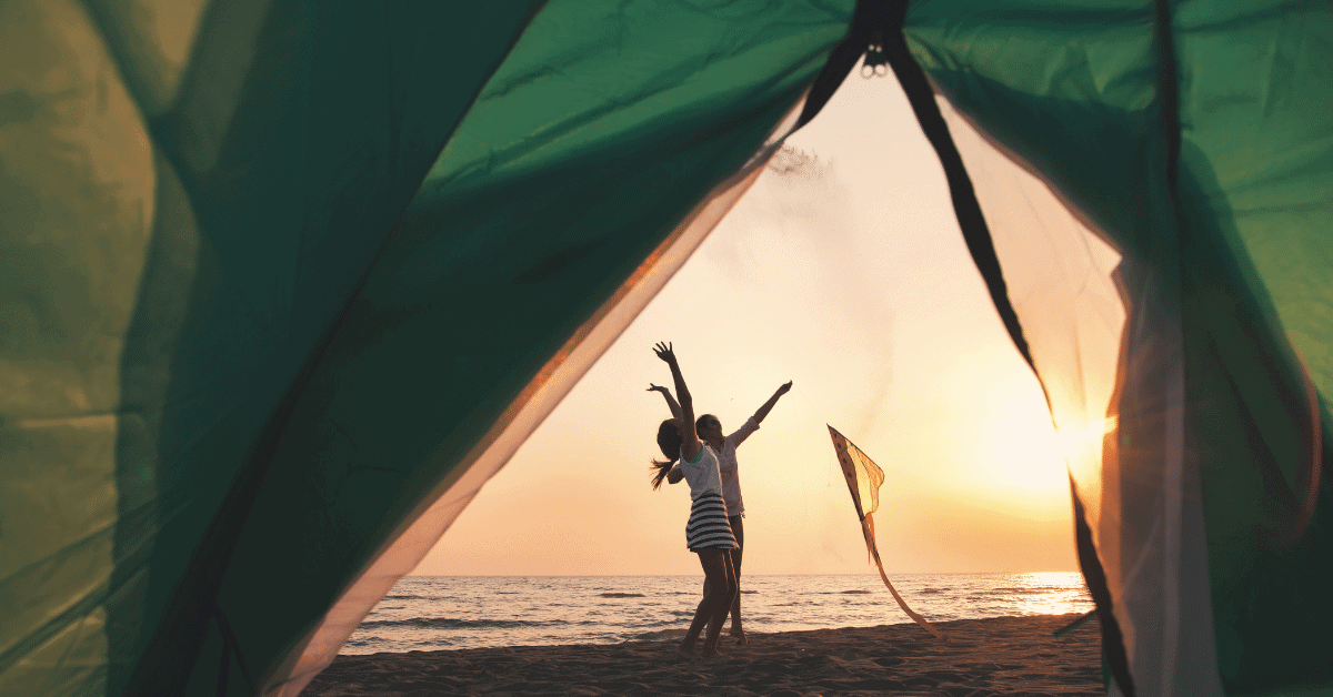 2 people on a beach in front of a tent