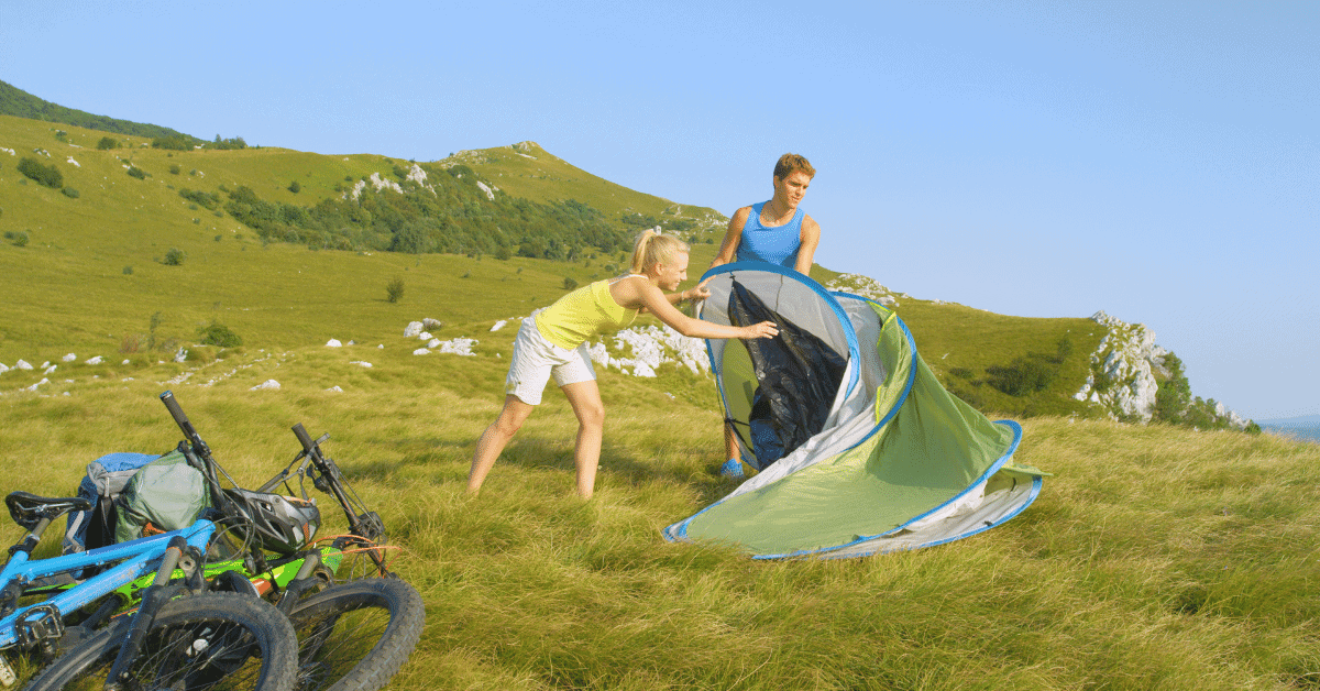 2 people unfolding a pop up tent on a hillside