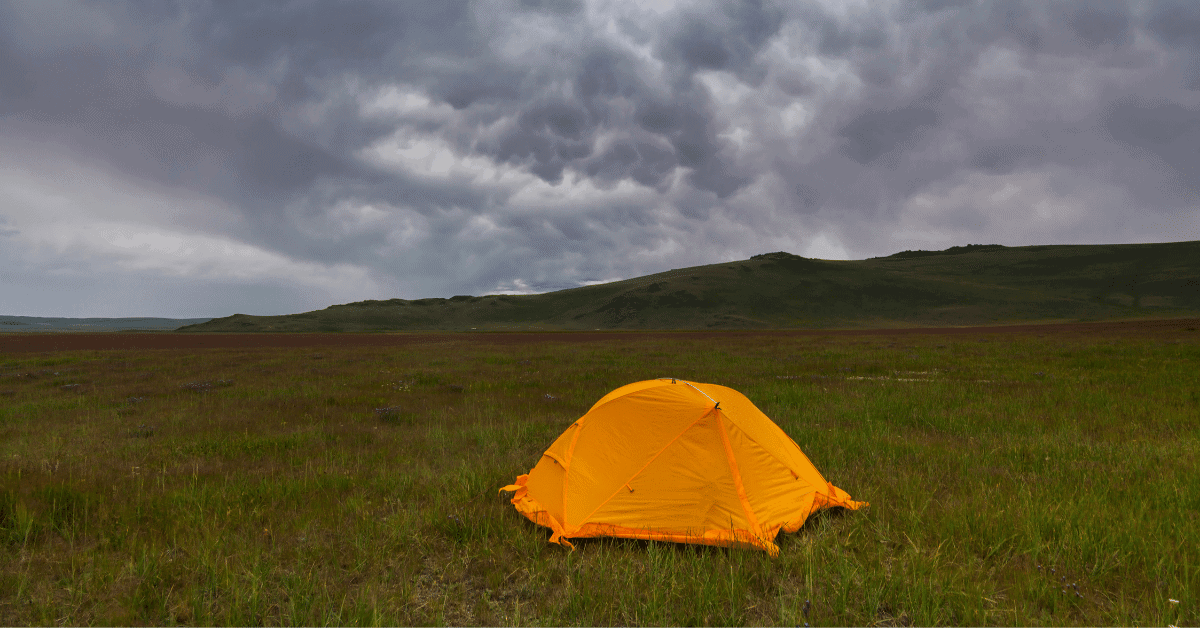 a tent in a field with grey cloudy skies above