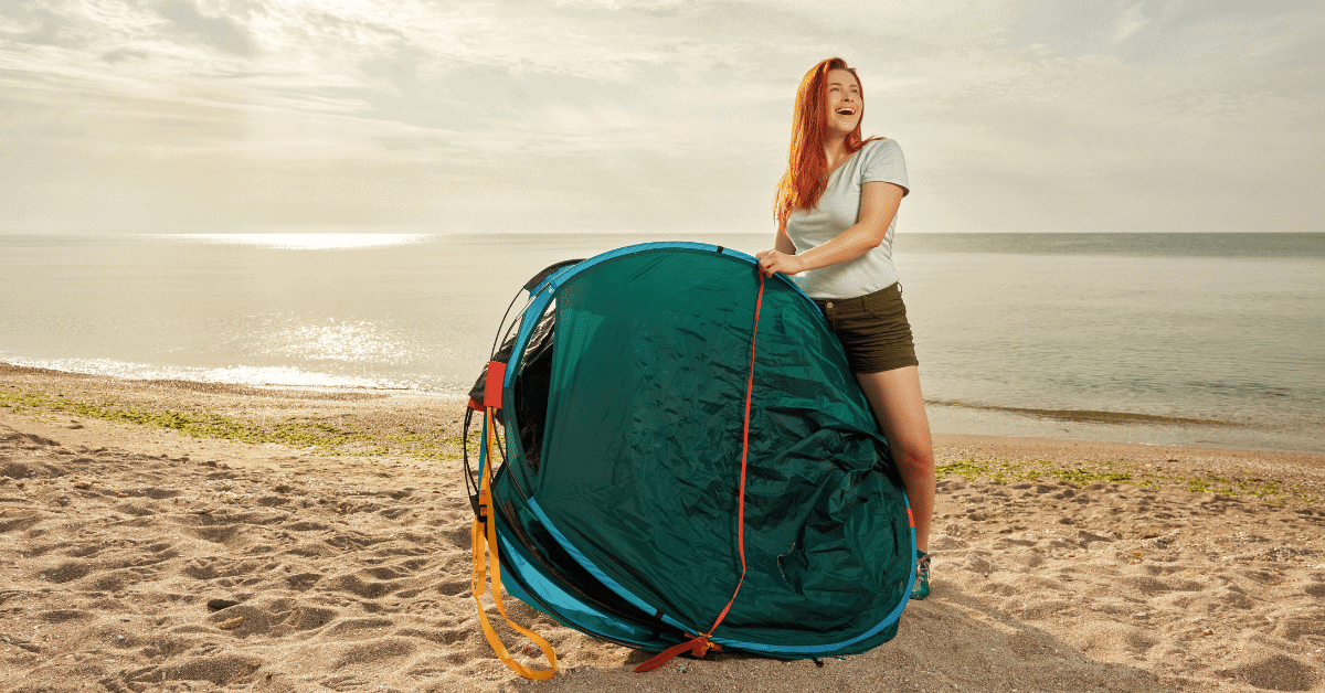 a woman on a beach holding a folded popup tent