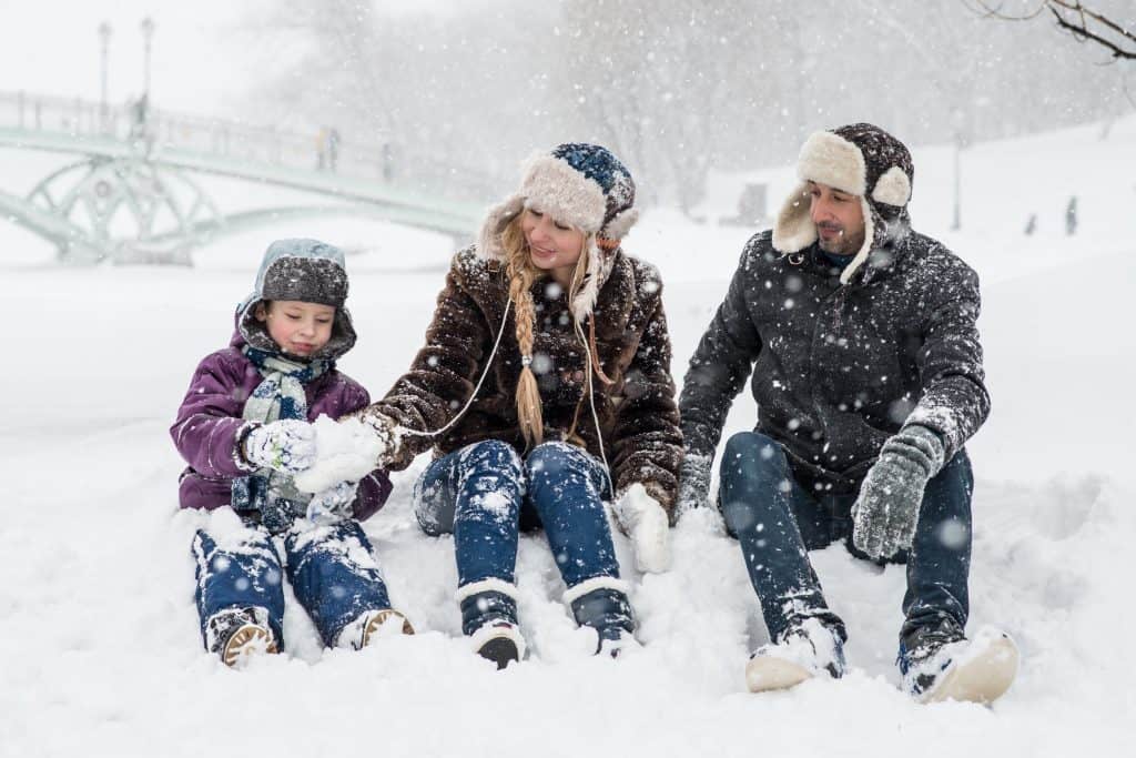 Woman, man, and girl sitting on snow