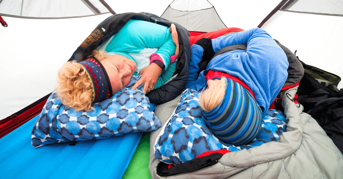 2 people in warm clothes and sleeping bags inside a tent