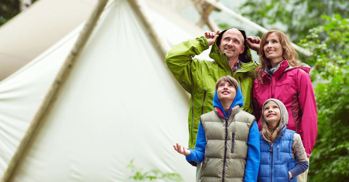 a family standing in front of a canvas tent in the rain