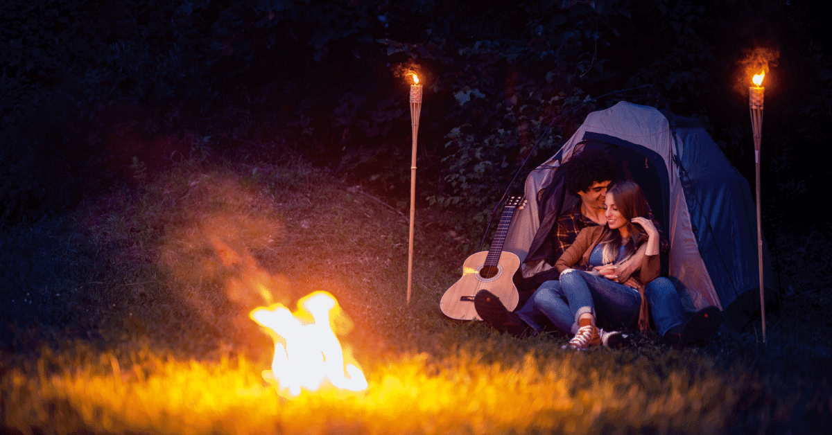 a couple in front of a tent with tiki torches and a campfire