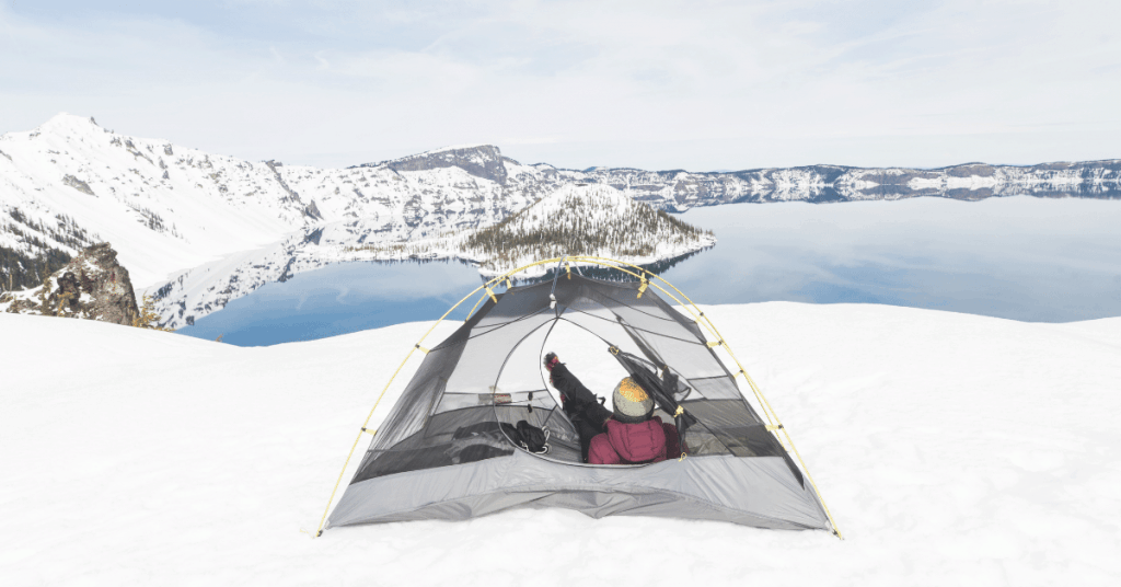 a person in a backpacking tent next to a snowy lake