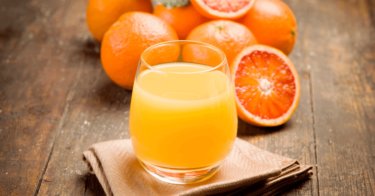 a glass of orange juice with orange halves in the background