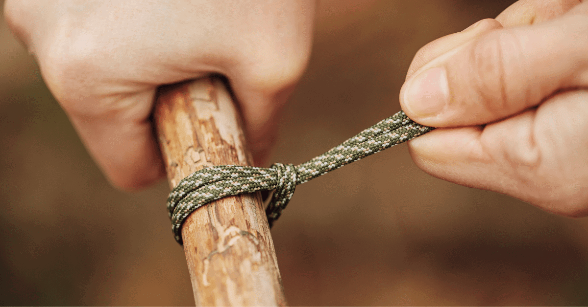 a pair of hands tying a piece of rope to a piece of wood