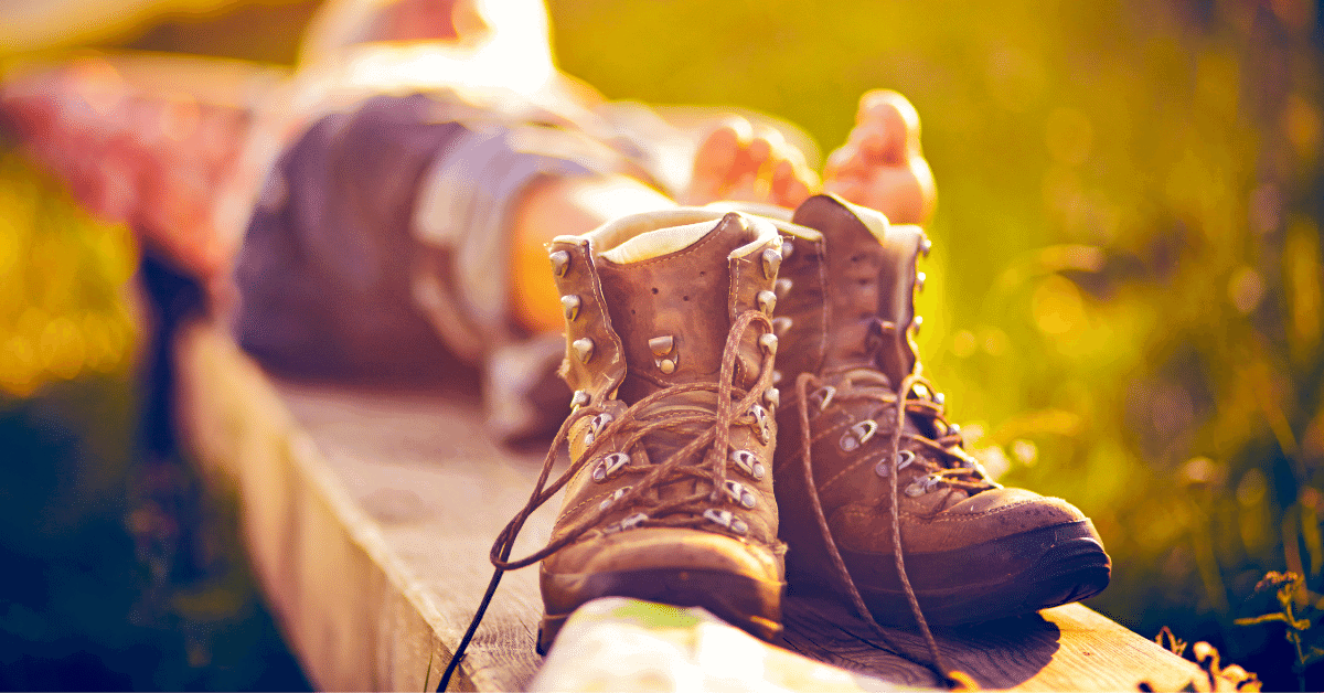 a pair of hiking boots with a barefoot hiker relaxing in the background