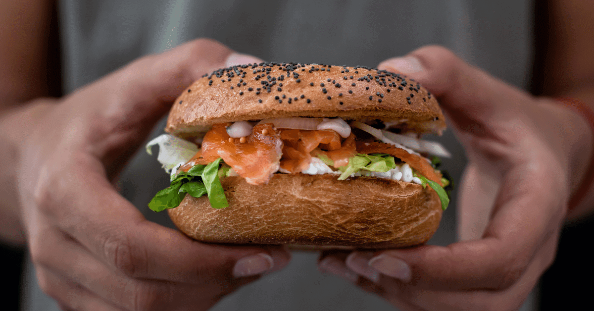 a person holding a lox and cream cheese bagel