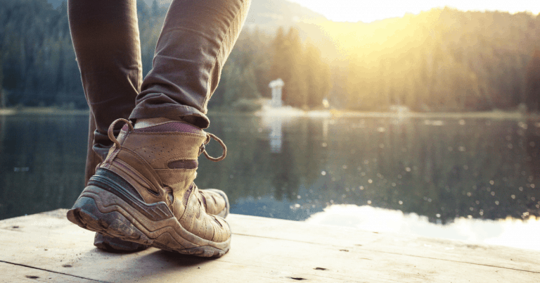a person wearing hiking boots next to a lake