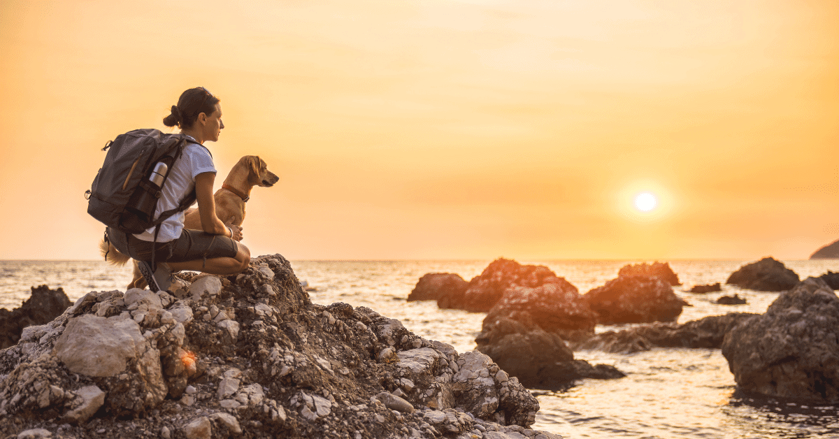 a woman and a dog taking a break on a hike by the sea