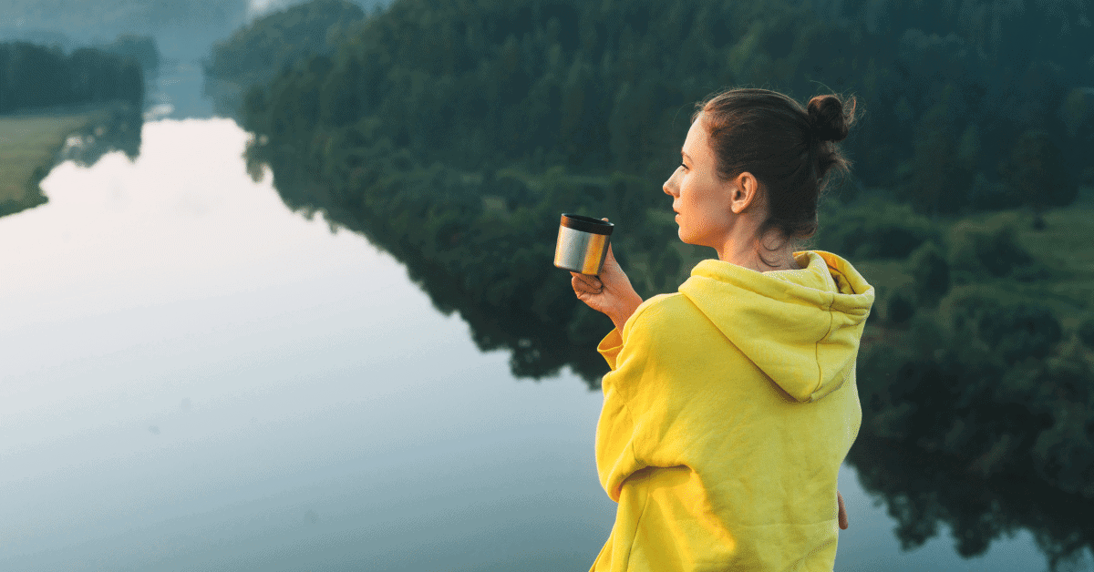 a woman drinking coffee by a river