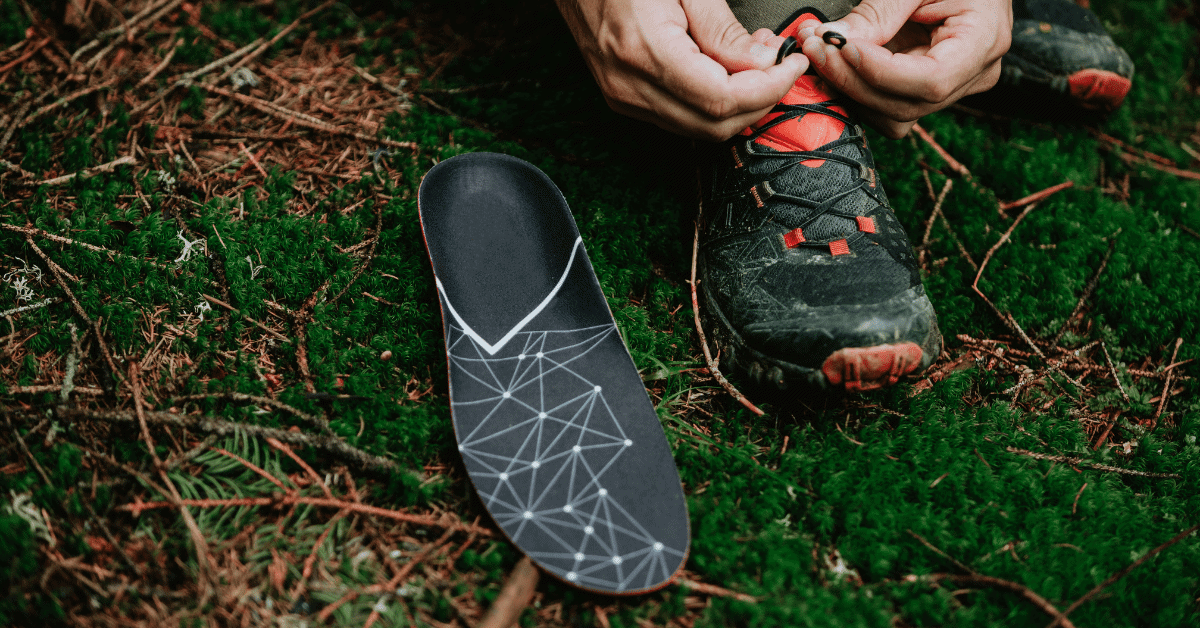 an orthotic on the grass next to a person tying the laces on their hiking shoes