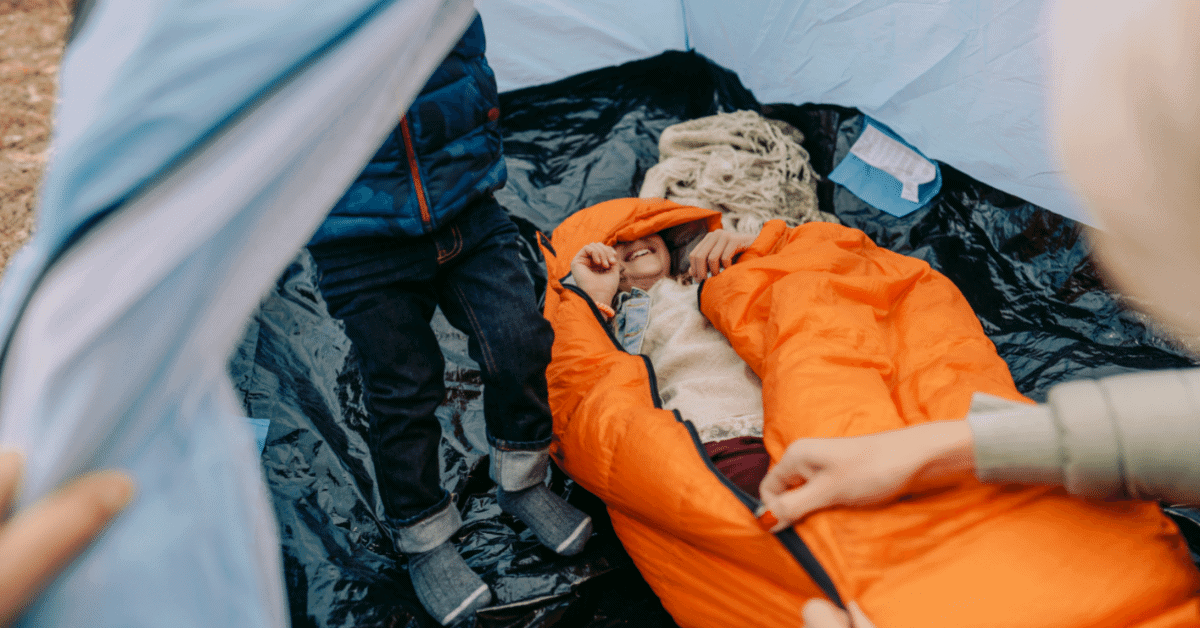 a kid in a mummy bag in a tent