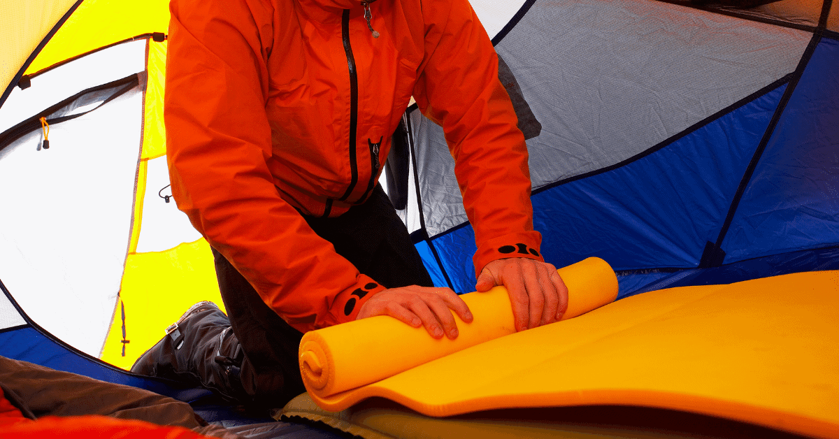 a man unrolling a sleeping pad in a tent