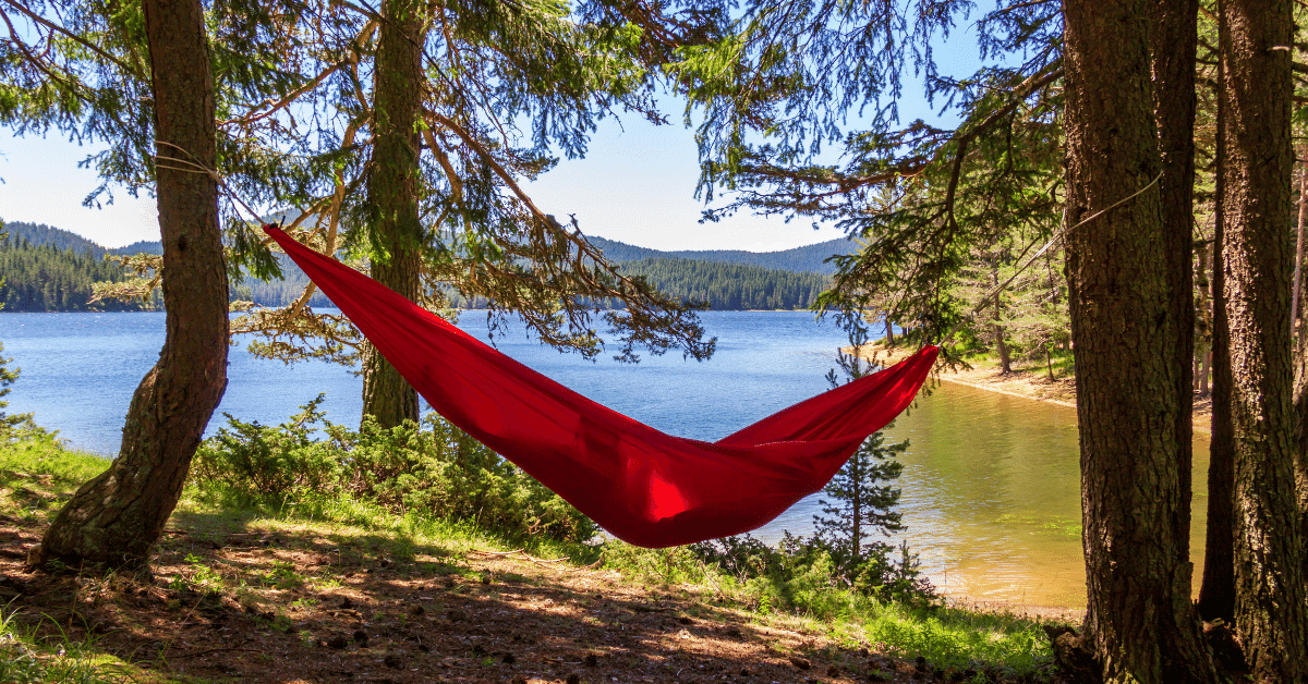 a person lying in a red hammock beside a lake