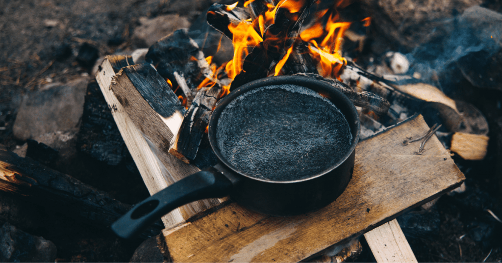 a pot of boiling water next to a campfire