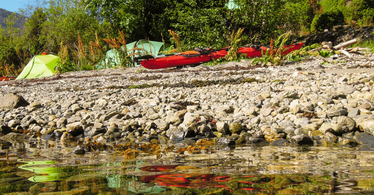 a red kayak next to a campsite on a riverbank