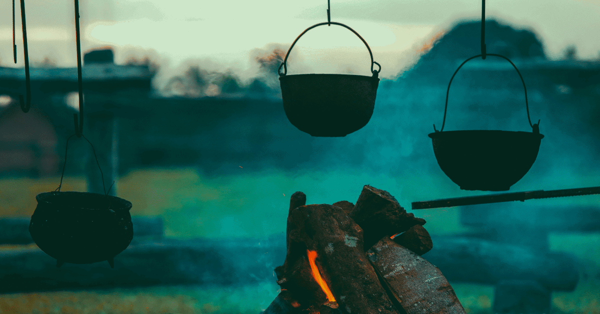 several pots hanging from a cowboy cooking stand