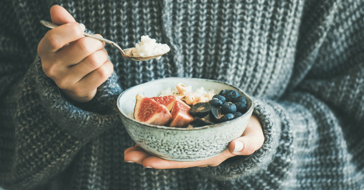 someone holding a bowl of porridge with figs and blueberries