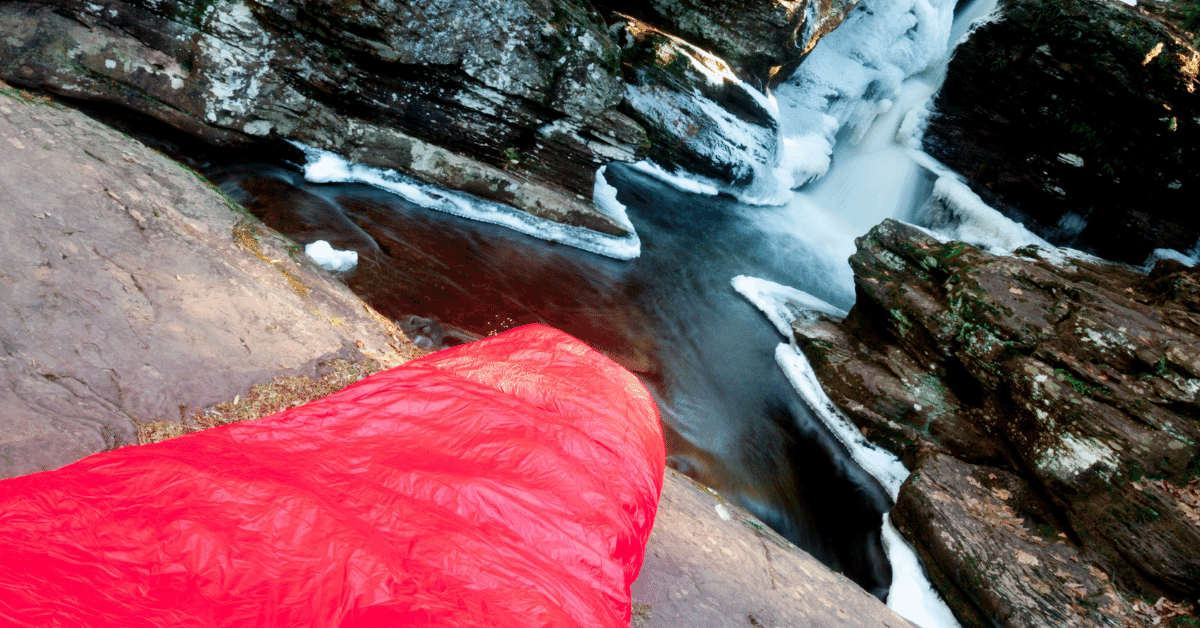 red sleeping bag next to a frozen waterfall