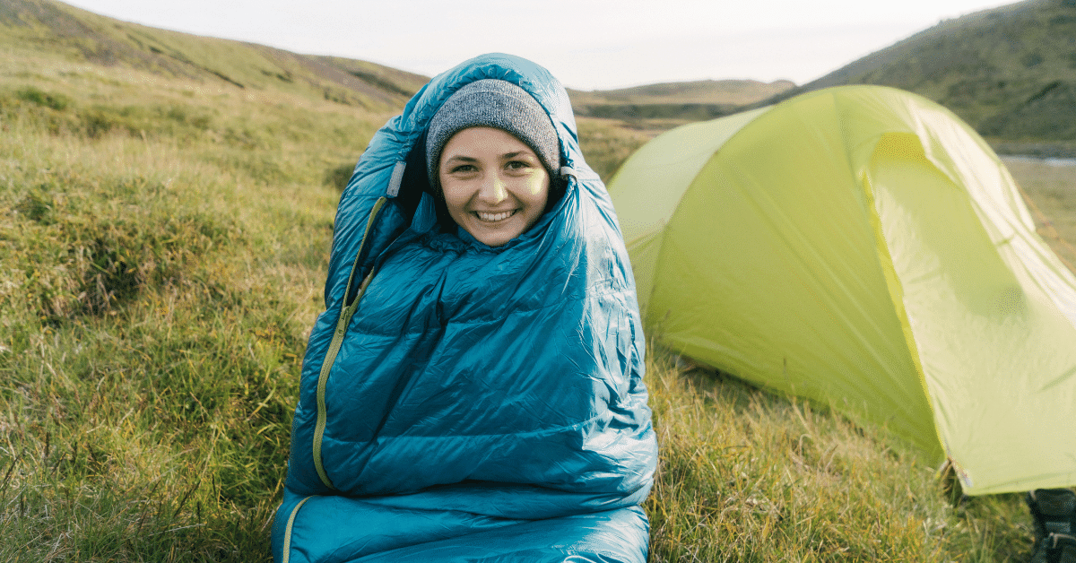 smiling girl in a blue sleeping bag in front of a green tent