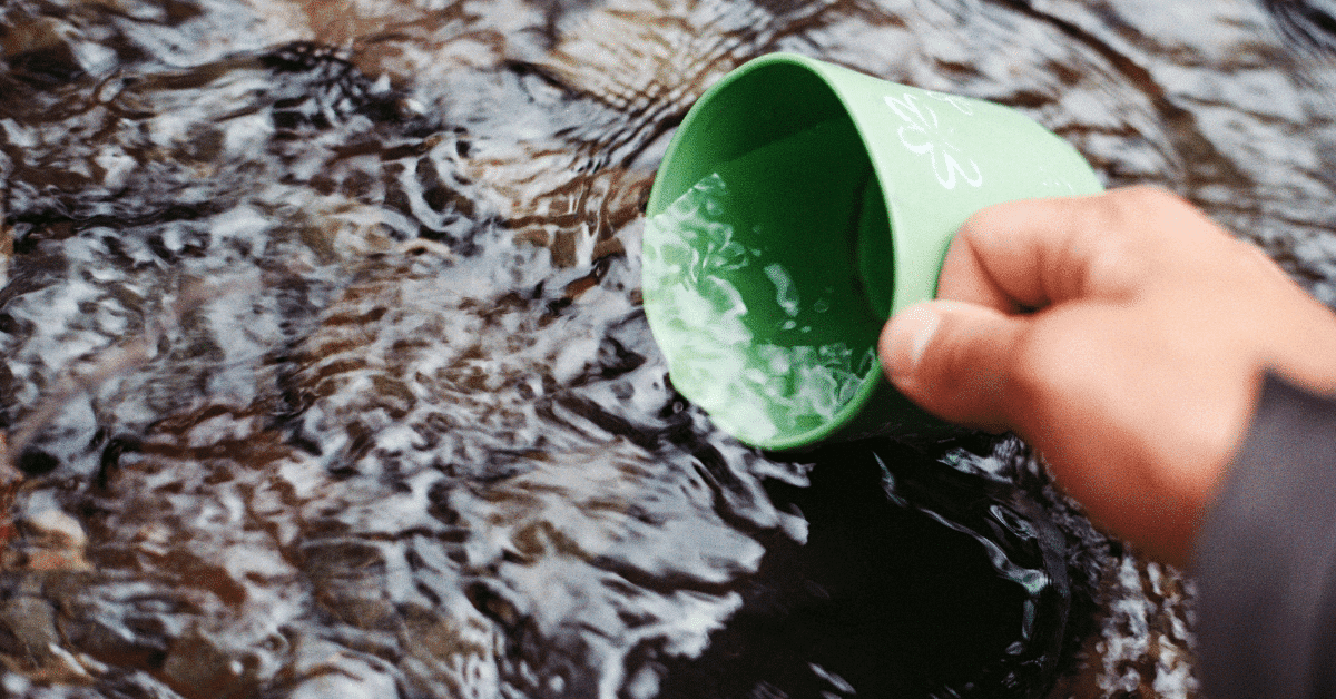 person collecting water from a steam in a green cup