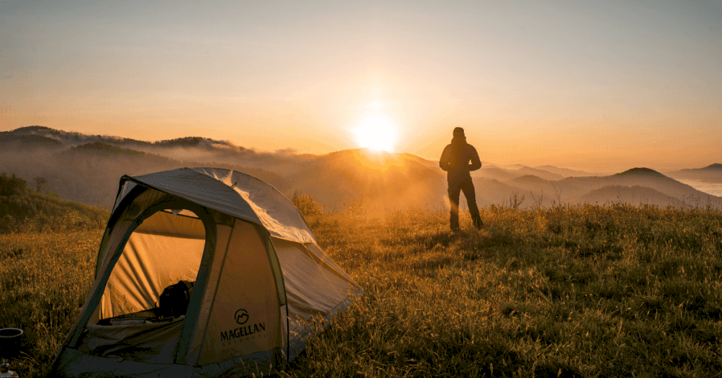 person standing in front of a tent in nature at sunset