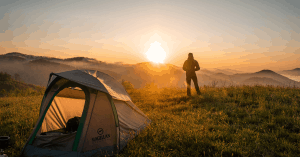 person standing in front of a tent in nature at sunset