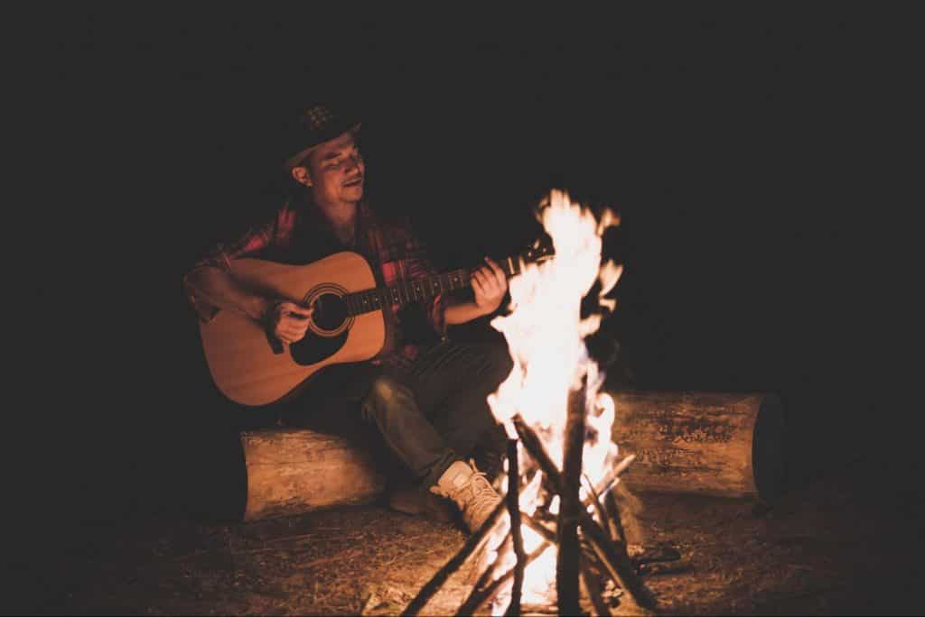 man playing guitar around the campfire