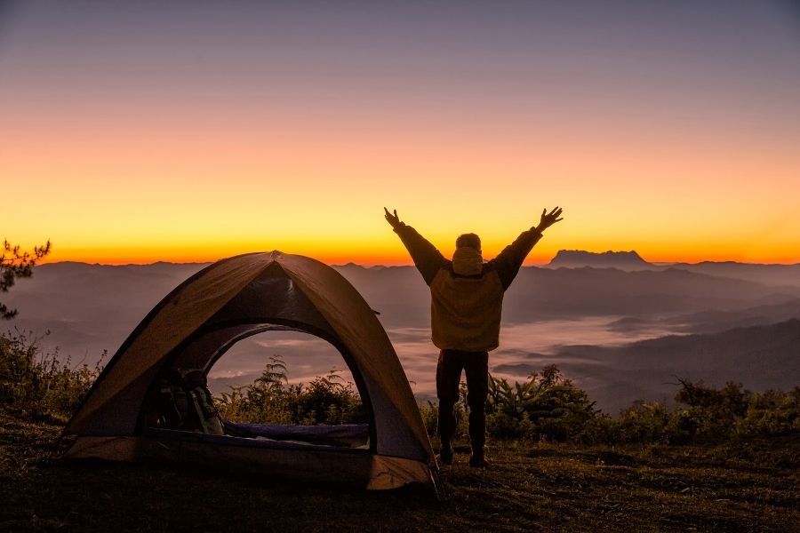 Man with arms open ventilating tent with beautiful view