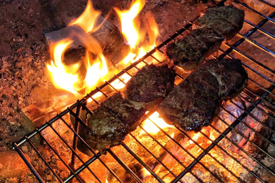 steaks being grilled over a campfire 