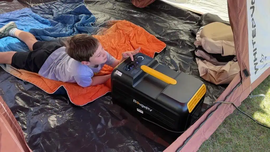 Campista extendiendo la mano para ajustar el aire acondicionado portátil BougeRV 3500BTU dentro de una tienda de campaña