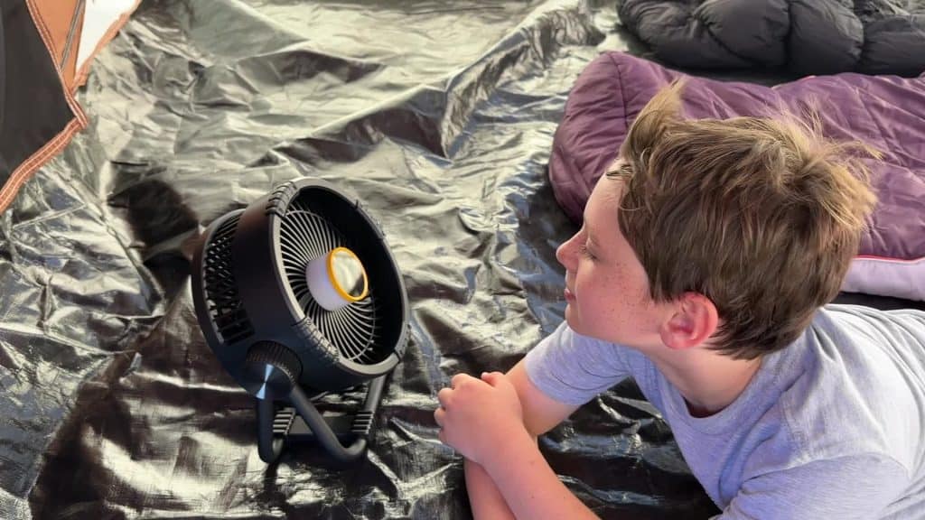 Campista utilizando el ventilador BougeRV F01 dentro de una tienda de campaña con saco de dormir