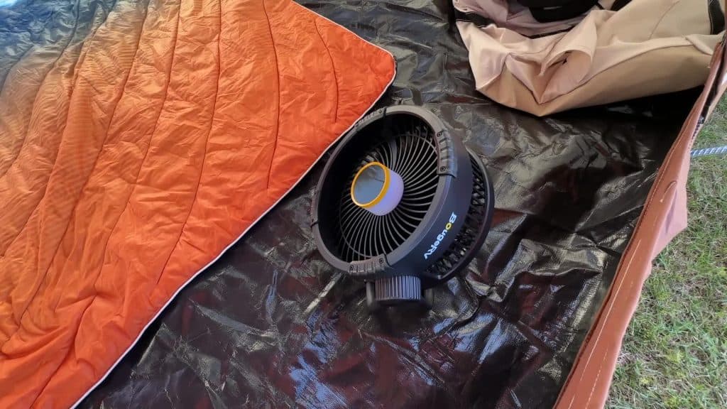 Ventilador BougeRV F01 colocado en una tienda de campaña junto a un saco de dormir naranja, que muestra la báscula y la configuración de la tienda