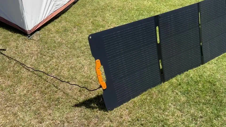 Panel solar plegable portátil UDPower de 210 W desplegado sobre el césped junto a una tienda de campaña con soporte extendido
